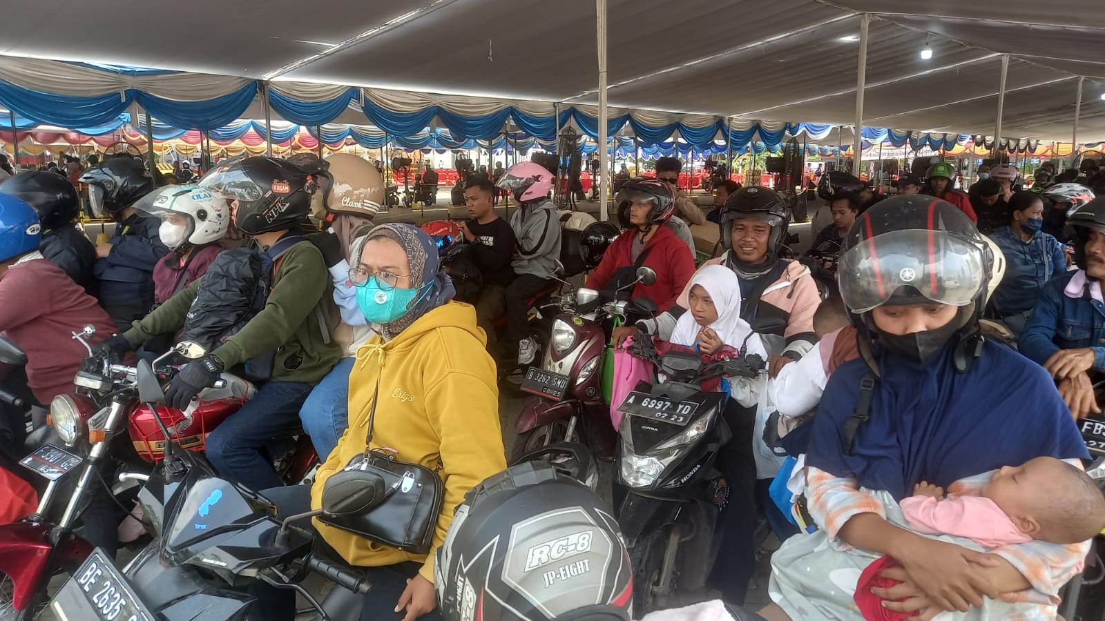 Seorang bayi tertidur dalam pelukan ibunya saat ikut berdesakan dalam antrian dijalur khusus pemudik menggunakan sepeda motor di Pelabuhan Ciwandan, Kota Cilegon, Kamis 20 April 2023 siang. (Foto: Daeng Yusvin)